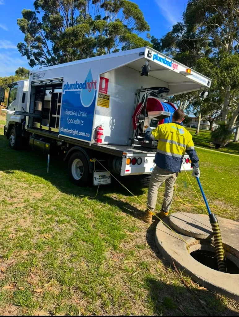 Plumbed Right jetting truck parked on grass while a plumber feeds a jetting hose into an open manhole