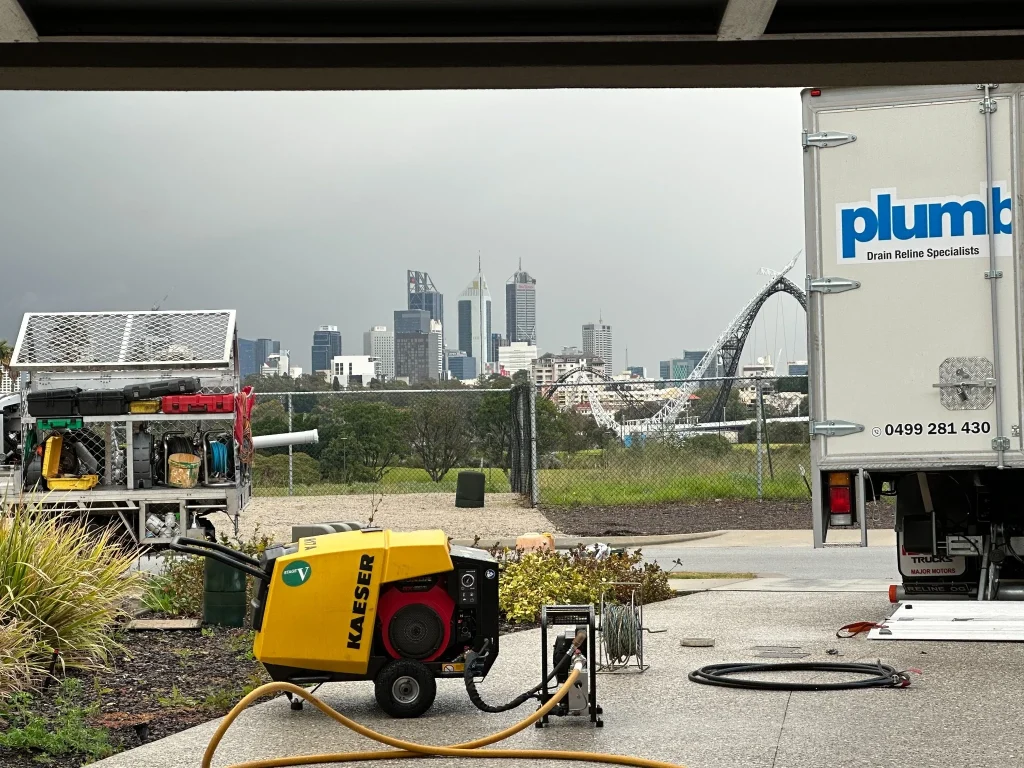 Plumbed Right drain relining truck and a compressor set up on a Perth job site with the city skyline behind