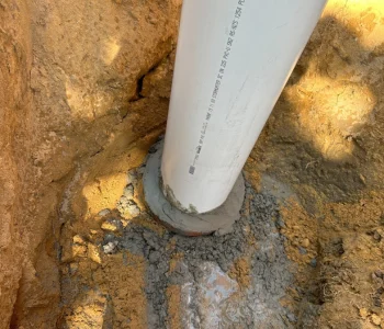 New PVC drain pipe set into a fresh concrete collar in an excavated trench