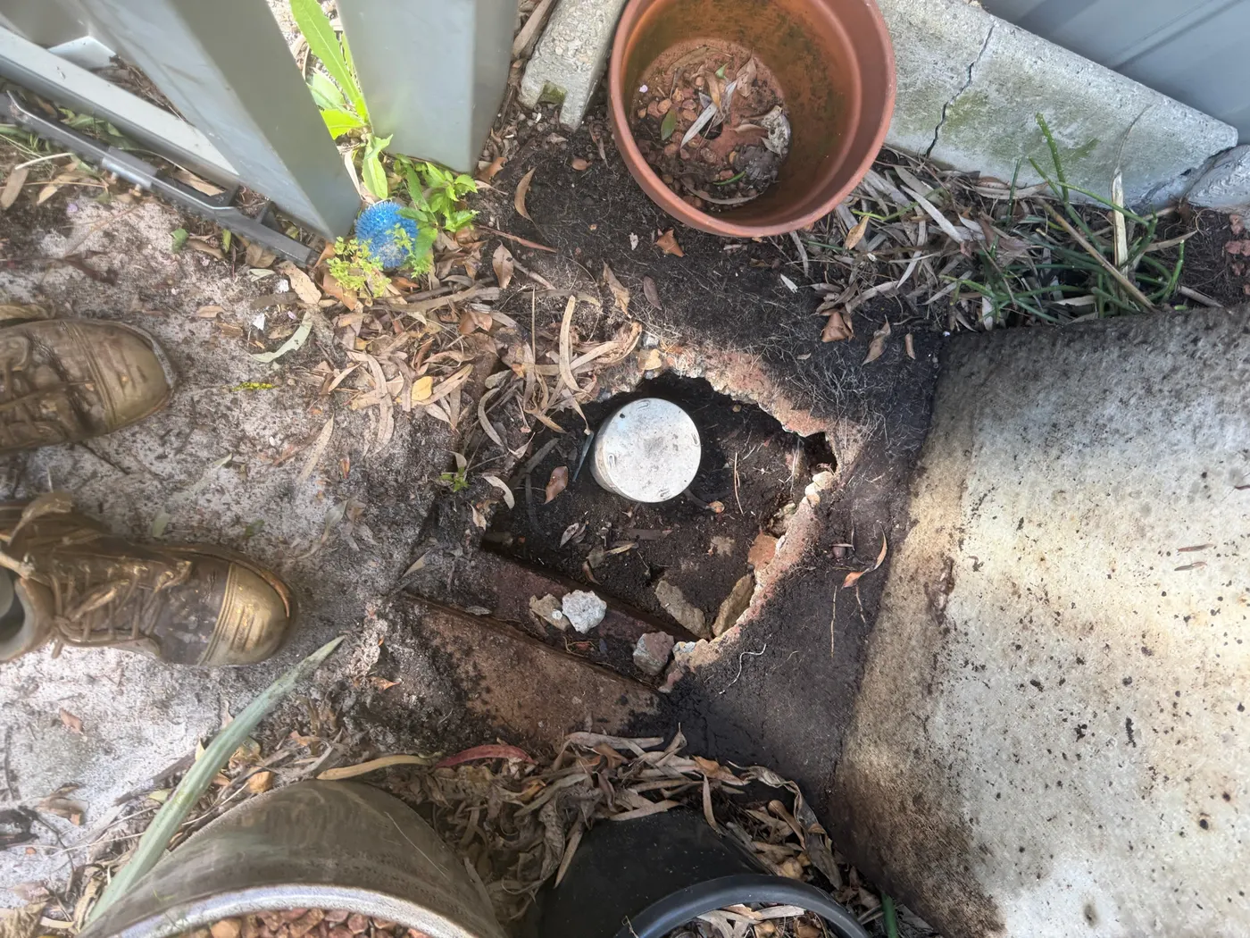 Drain inspection opening dug out beside a concrete path in a back garden