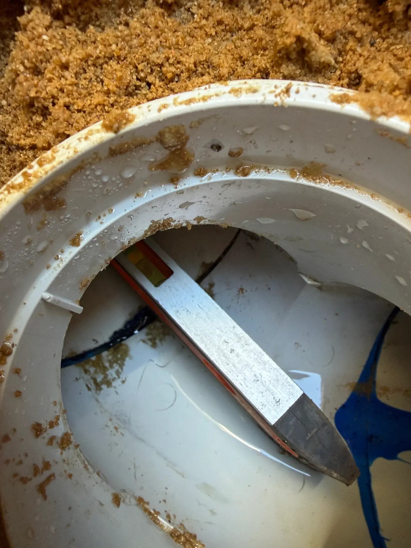PVC drain fitting dug out of yellow sand and opened up to reach a blocked branch line