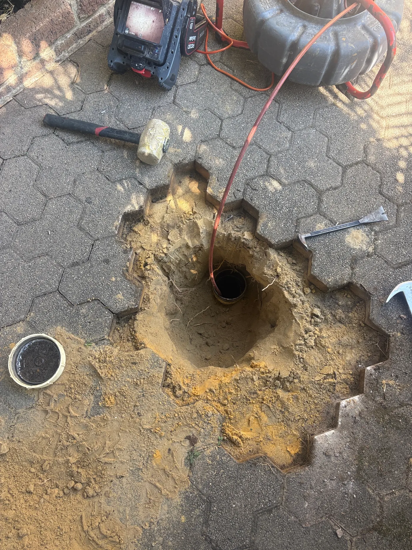 Paving cut back and sand dug out to an exposed drain pipe, with the CCTV camera cable fed in and the monitor beside it