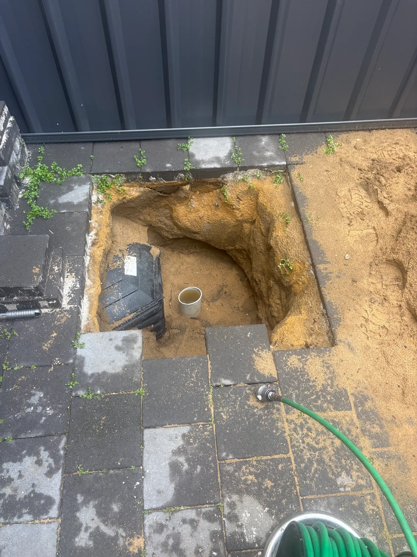 Hole dug through sand under pavers to reach a sewer riser at a Heathridge job