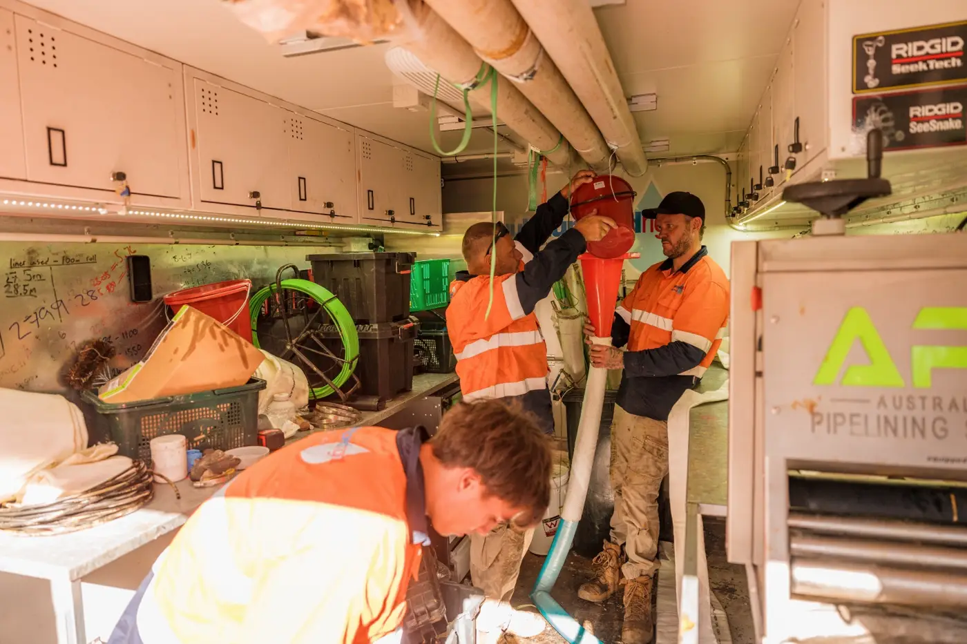 Three techs in hi-vis inside a relining rig trailer
