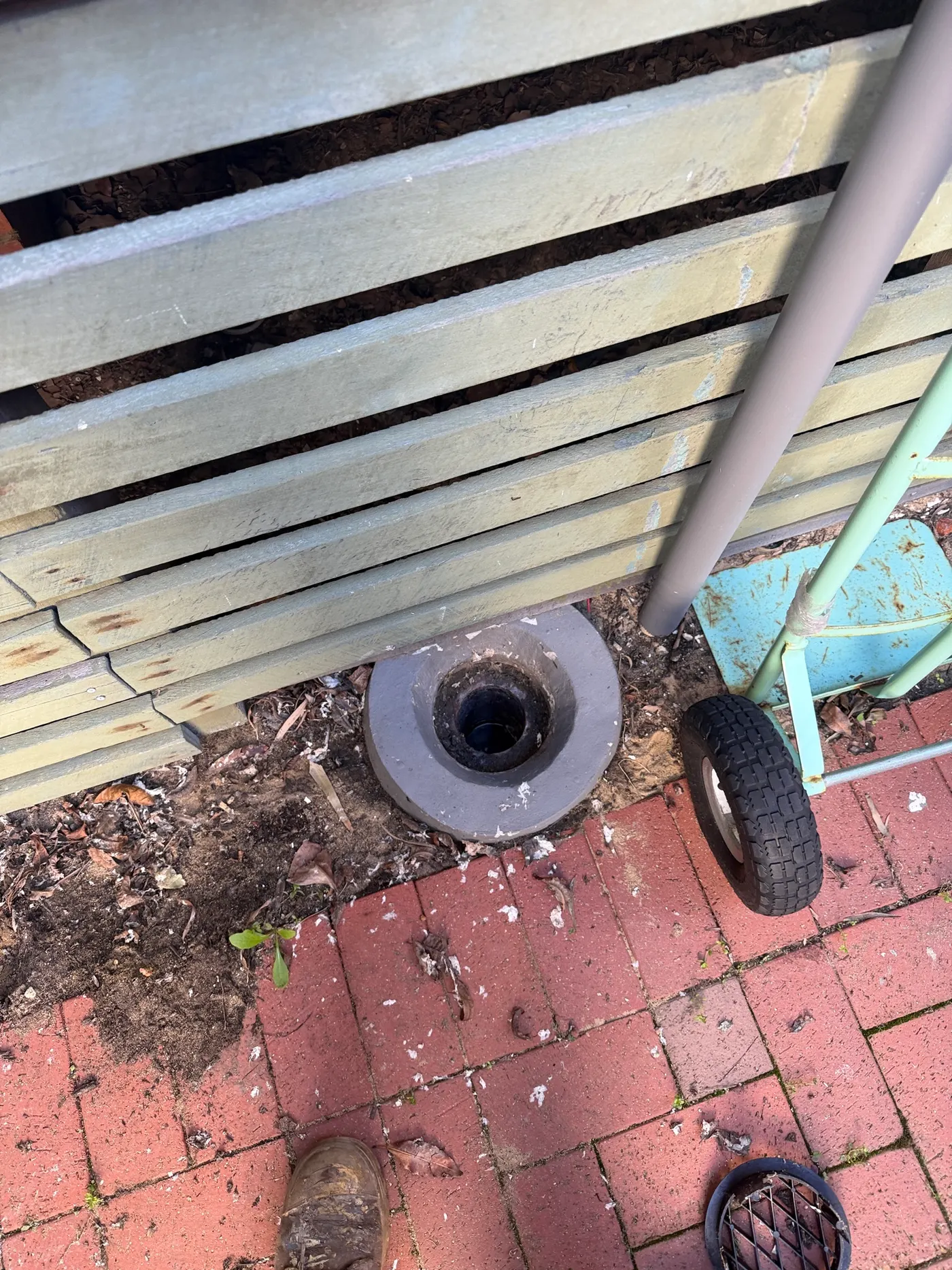 Sewer inspection shaft opened beside a garden fence and red brick paving