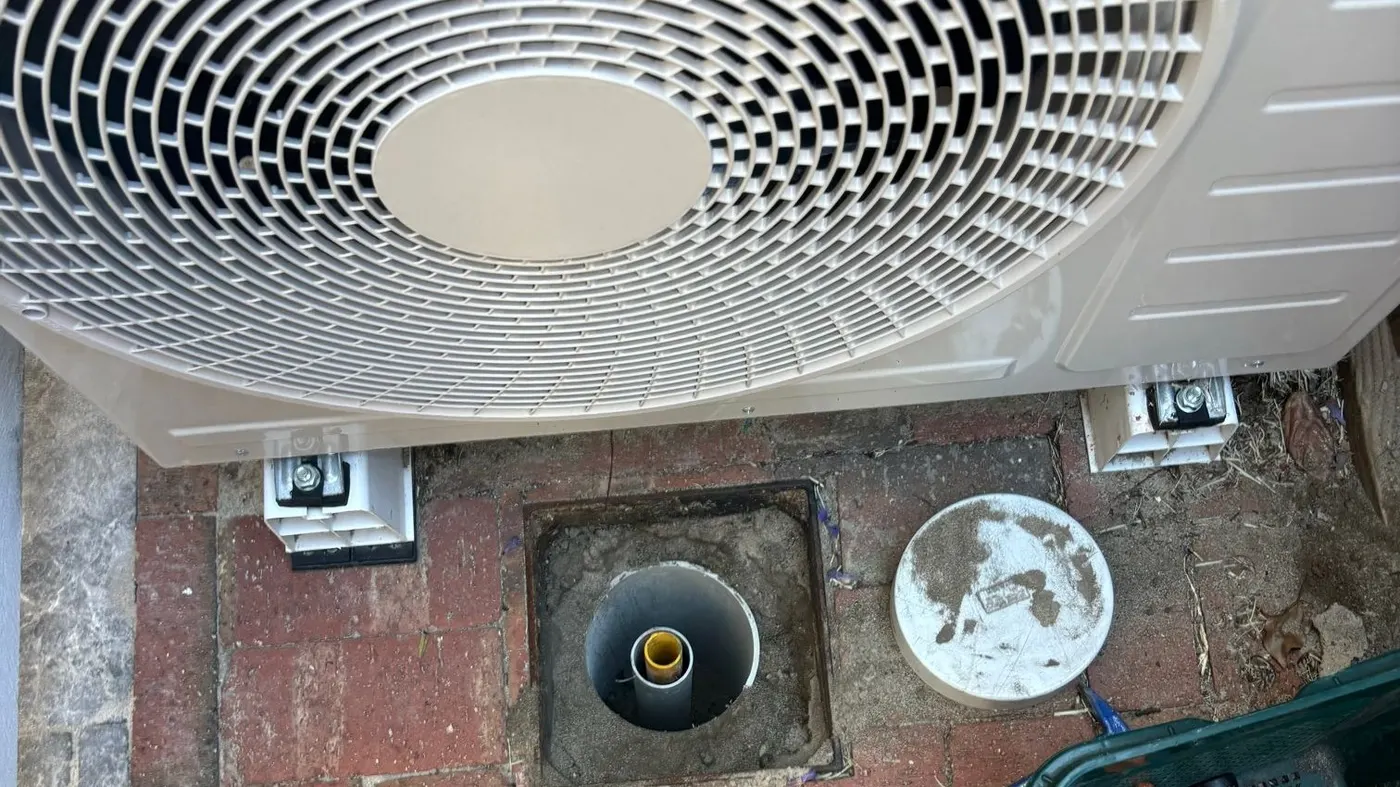 Exposed reflux valve riser in brick paving directly beneath an air conditioner unit at a Subiaco home