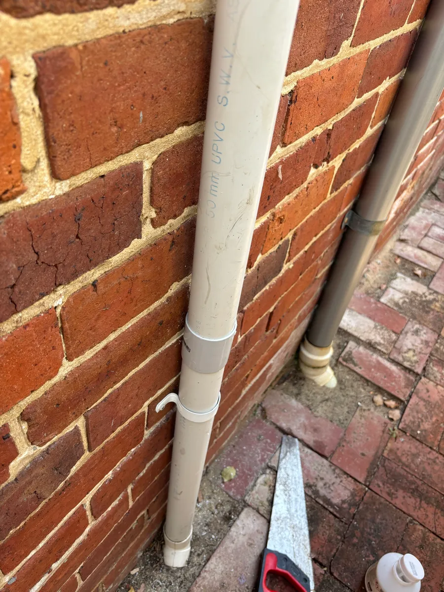 50 mm PVC vent pipe running up a brick wall in Subiaco, with a handsaw on the paving below