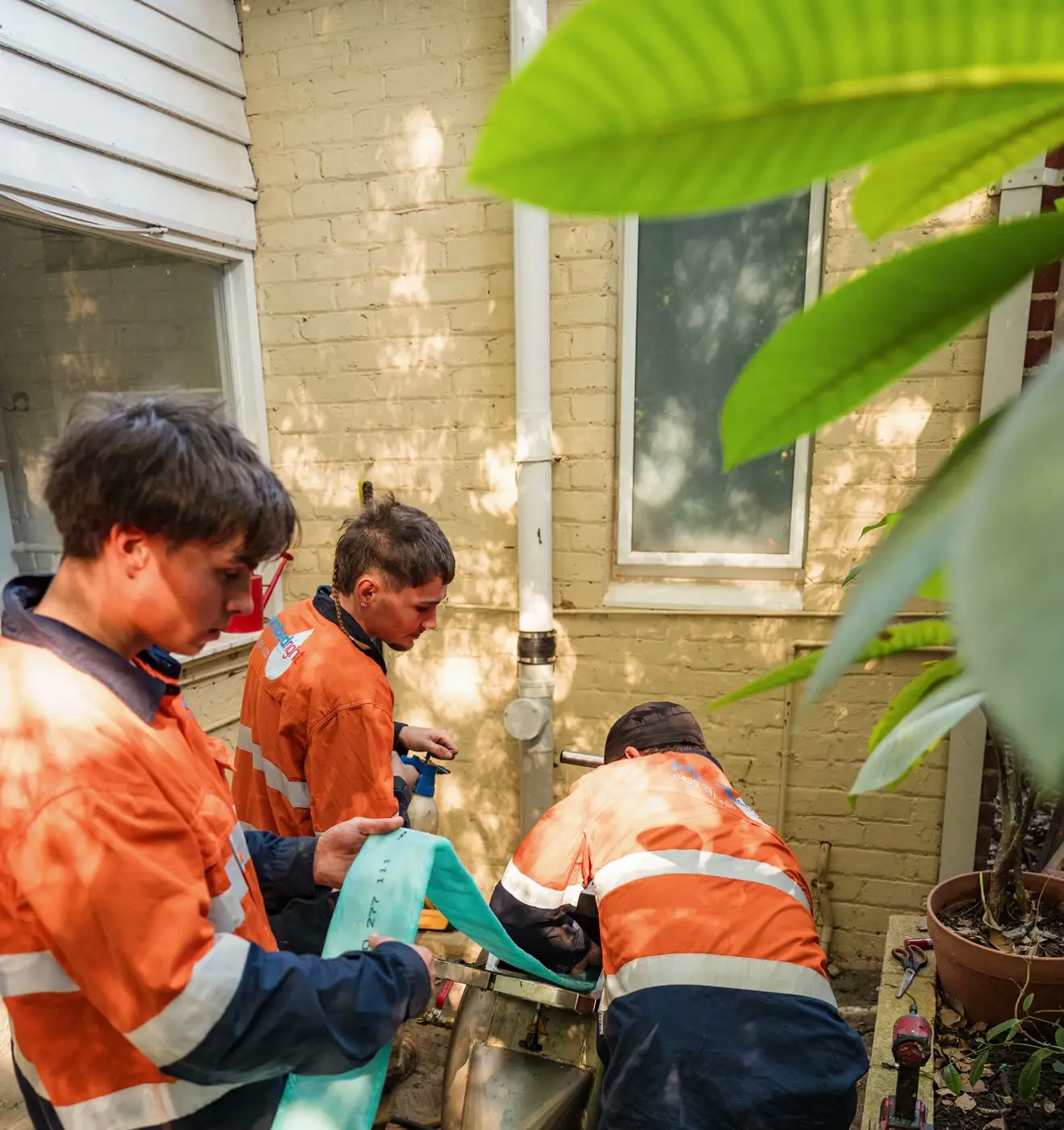 Three Plumbed Right techs at a drain beside a brick house