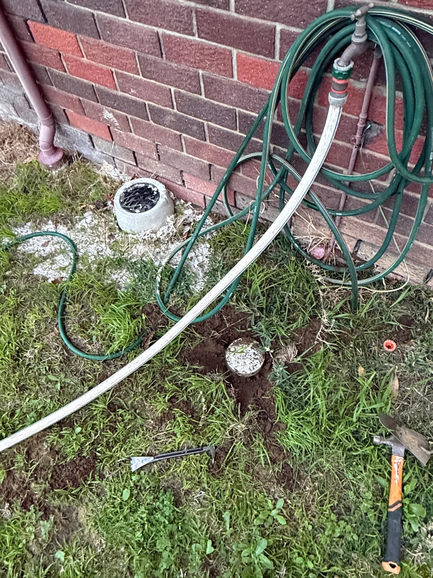 Drain gully and a dug-out cleanout point by a brick wall at a Wanneroo job